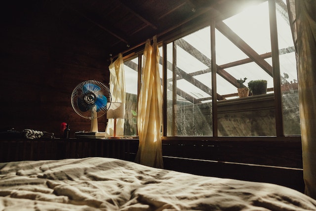 A bedroom with sunlight filtering in through the window, and a fan blowing cool air in